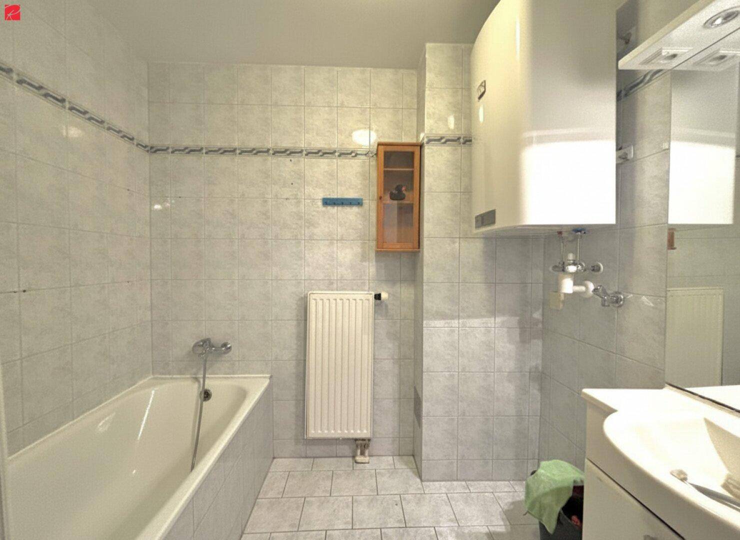 Helles Badezimmer mit Badewanne, Fliesenboden und Wandfliesen in neutralen Farben.