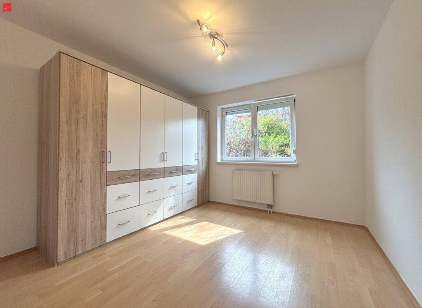 Geräumiges Schlafzimmer mit hellem Parkettboden und großem Einbauschrank, gut beleuchtet durch ein Fenster.