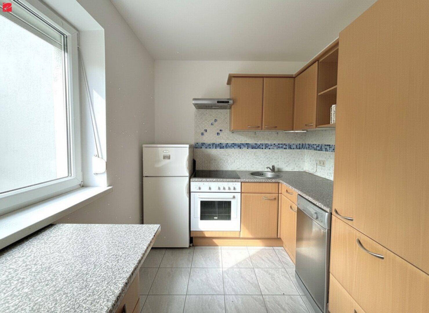 Funktionale Küche mit hellen Holzschränken, Fliesenboden und grundlegenden Küchengeräten.