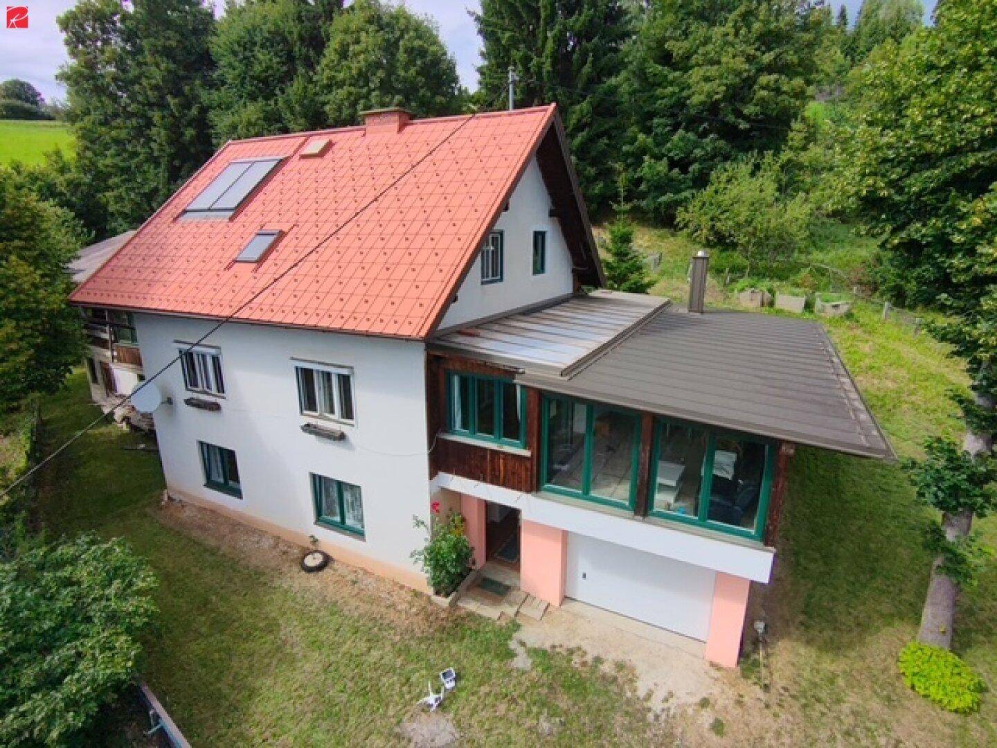 Seitenansicht des Hauses mit einem angebauten Wintergarten und einer Garage, eingebettet in eine grüne Hügellandschaft.