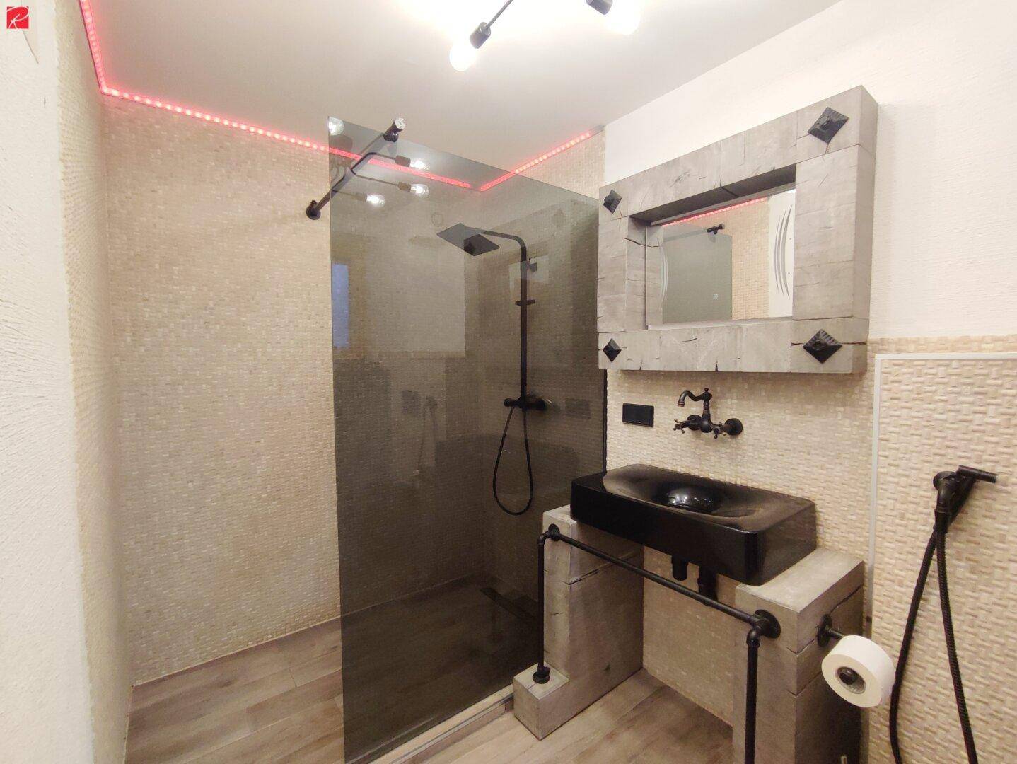 Modernes Badezimmer mit begehbarer Dusche, einzigartigem Waschbecken und hellen Fliesen.