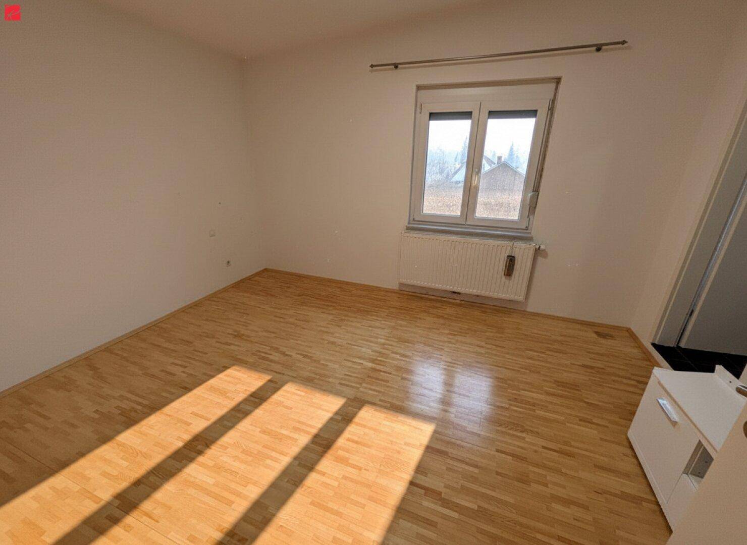 Leeres Schlafzimmer mit hellem Holzfußboden, weiß gestrichenen Wänden und Fenster.