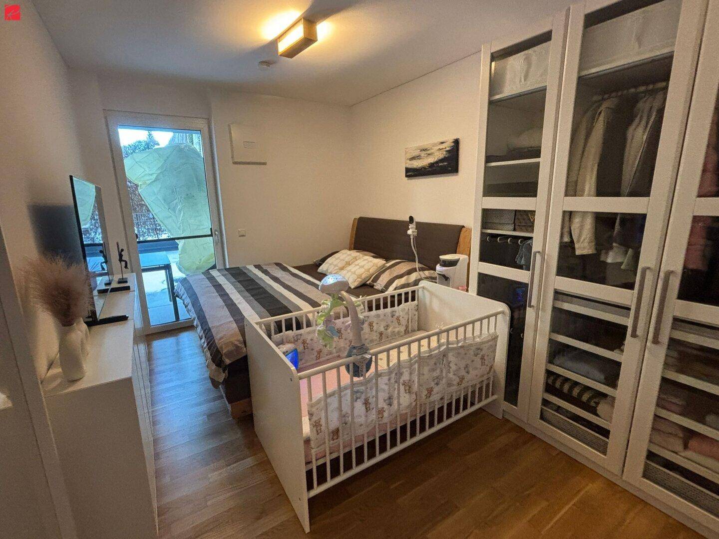 Schlafzimmer mit Doppelbett, Babybett und großem Kleiderschrank mit Balkonzugang.
