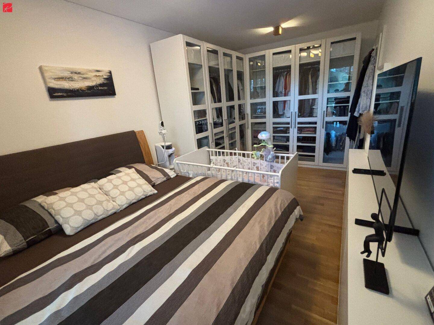 Geräumiges Schlafzimmer mit Doppelbett, Babybett und integriertem Kleiderschranksystem.