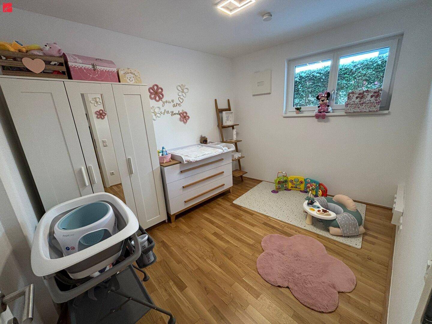 Helles Kinderzimmer mit Wickelkommode, Schrank und Spielteppich.