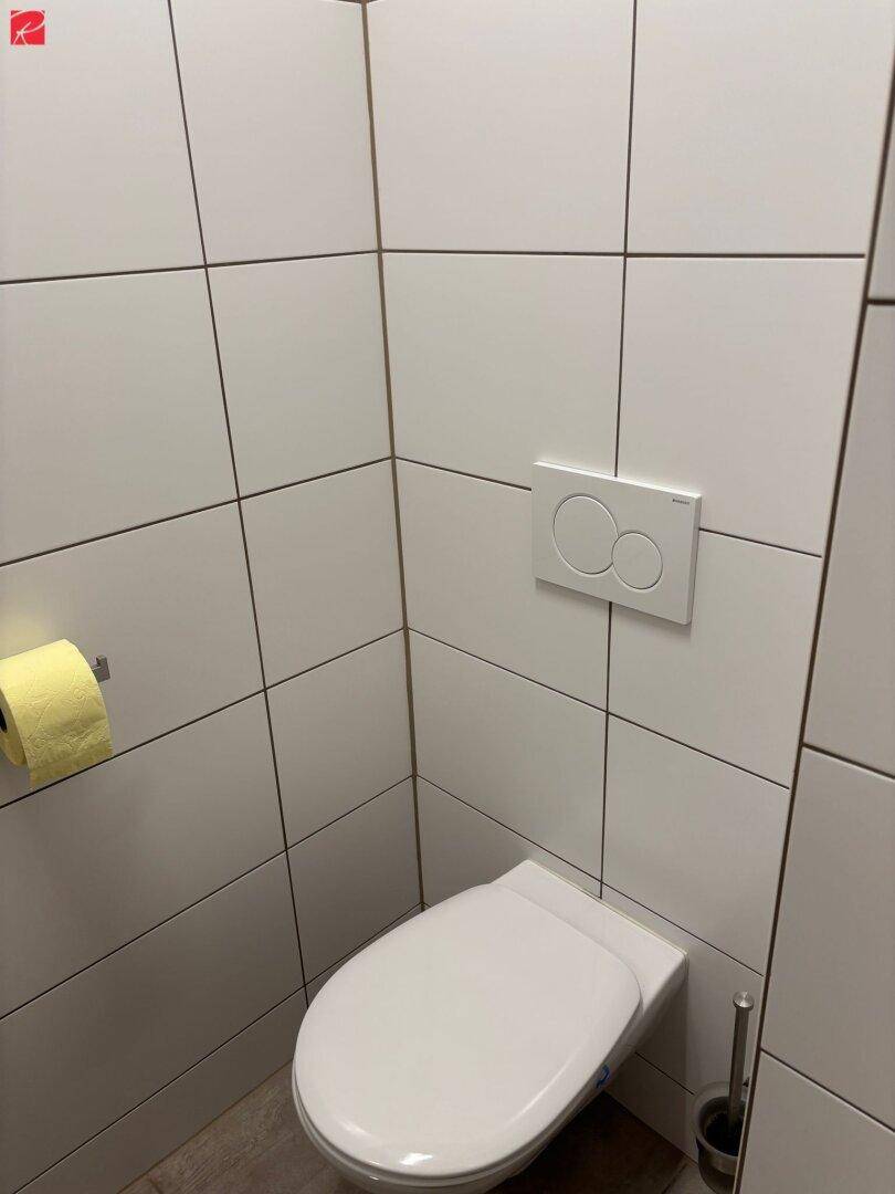 Separate Toilette mit Wand-WC und weißen Fliesen.