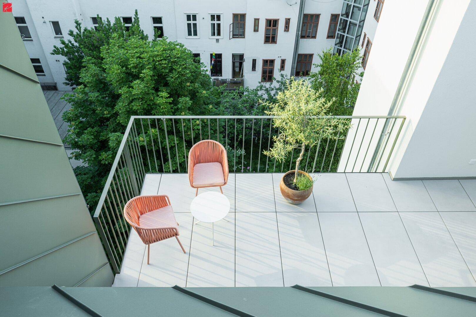 Heller Balkon mit modernen Fliesen, Sitzgelegenheiten und Blick ins Grüne.