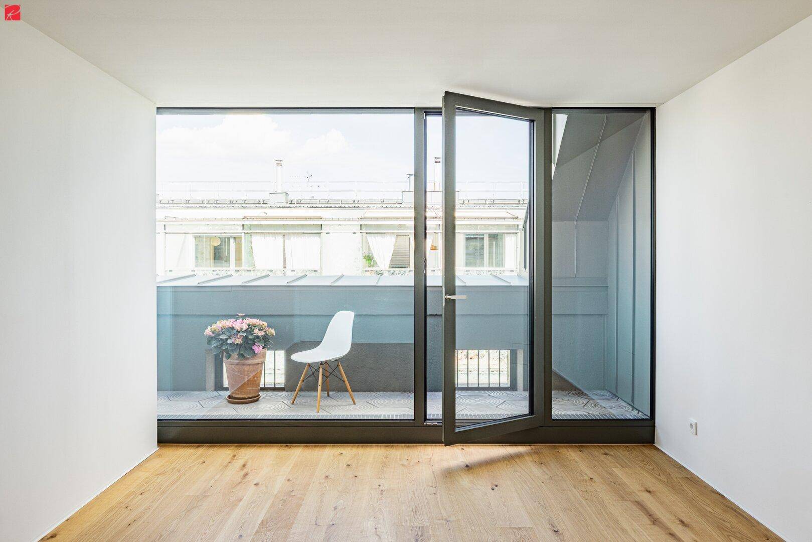 Heller Raum mit Holzboden und großem Fenster, das zu einem französischen Balkon führt.