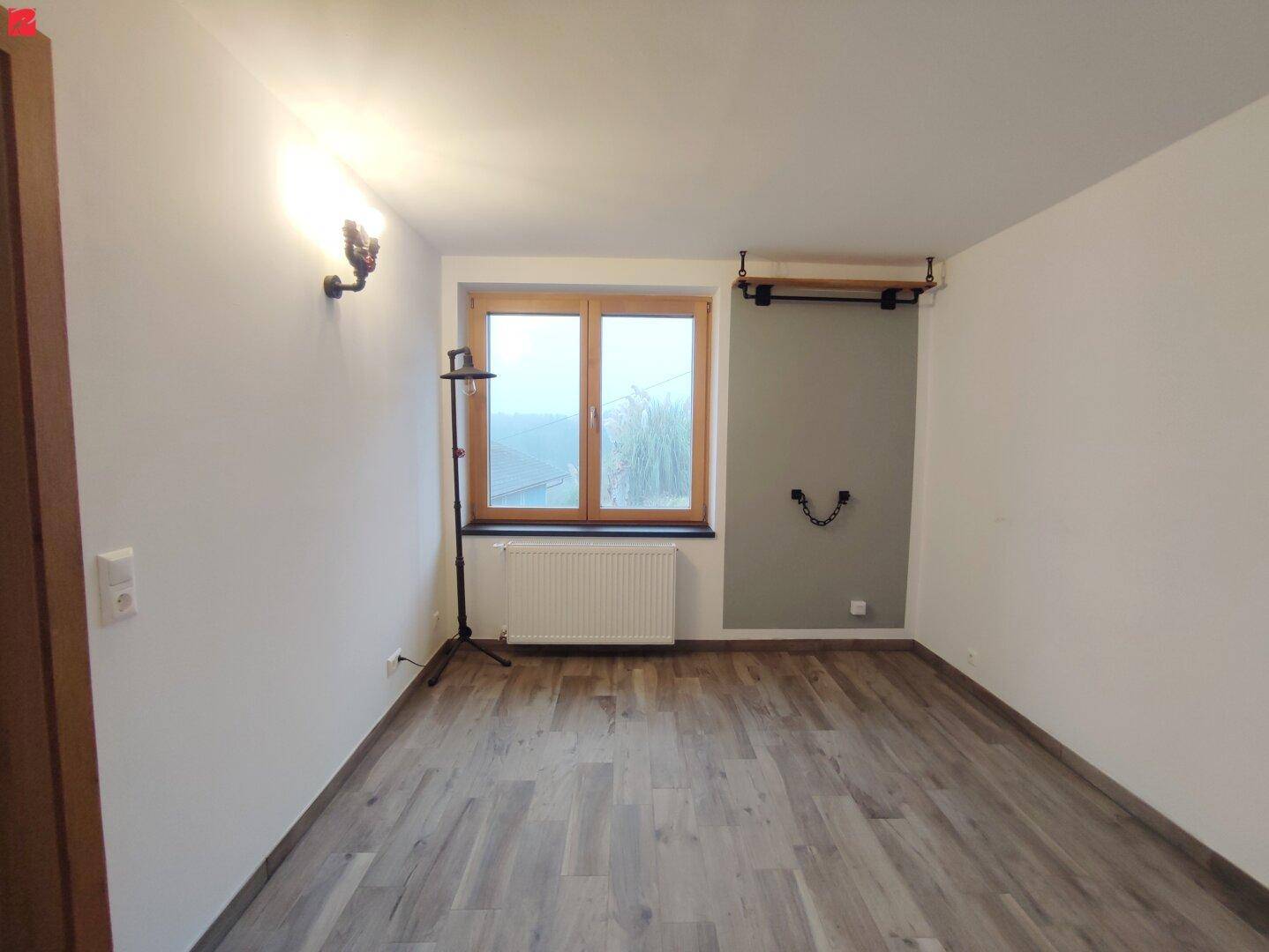 Leeres Zimmer mit Laminatboden und Fenster, ideal als Schlaf- oder Arbeitszimmer.