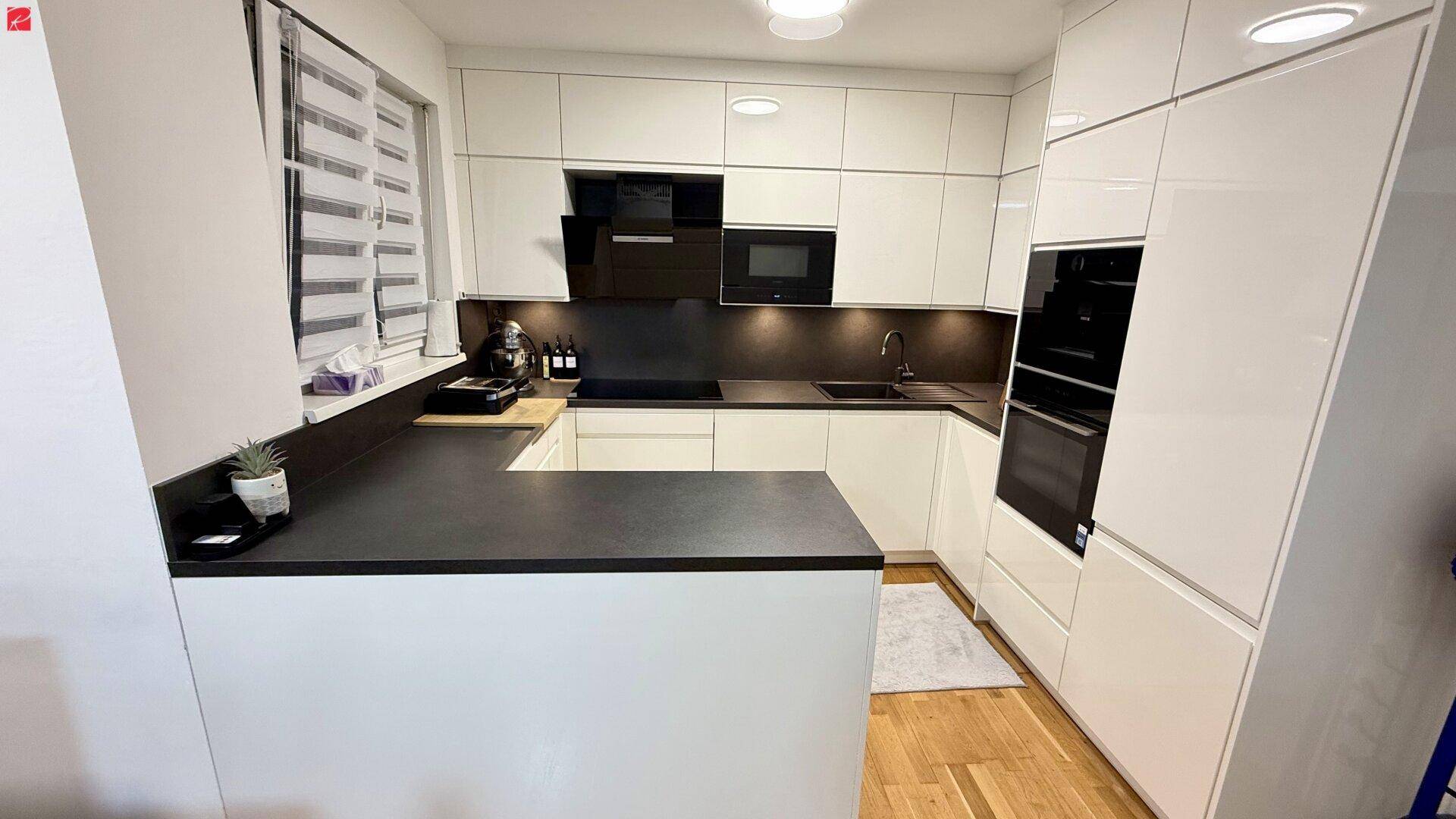 Moderne Einbauküche mit weißen Hochglanzfronten, dunkler Arbeitsplatte und integrierten Geräten.