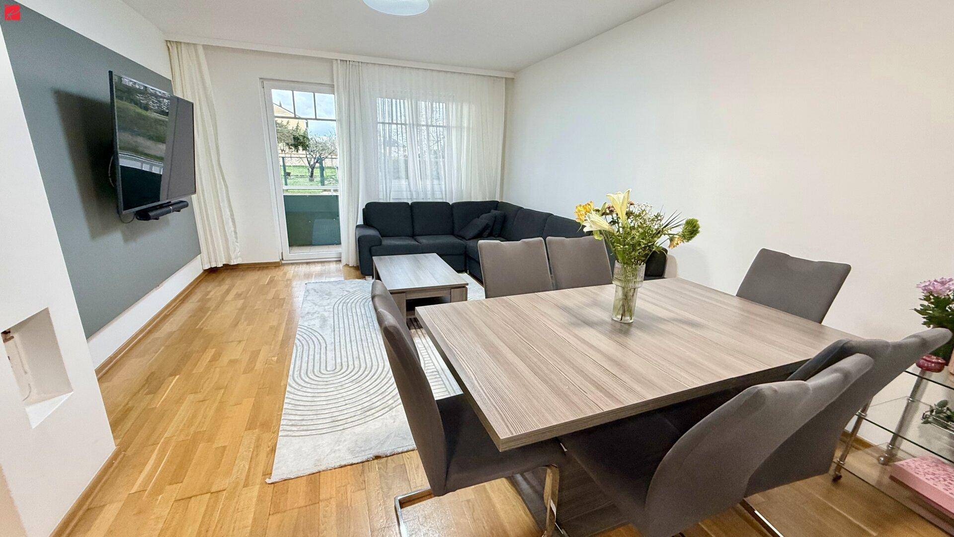 Heller Wohn- und Essbereich mit Holzboden, gemütlichem Sofa und Zugang zum Balkon.