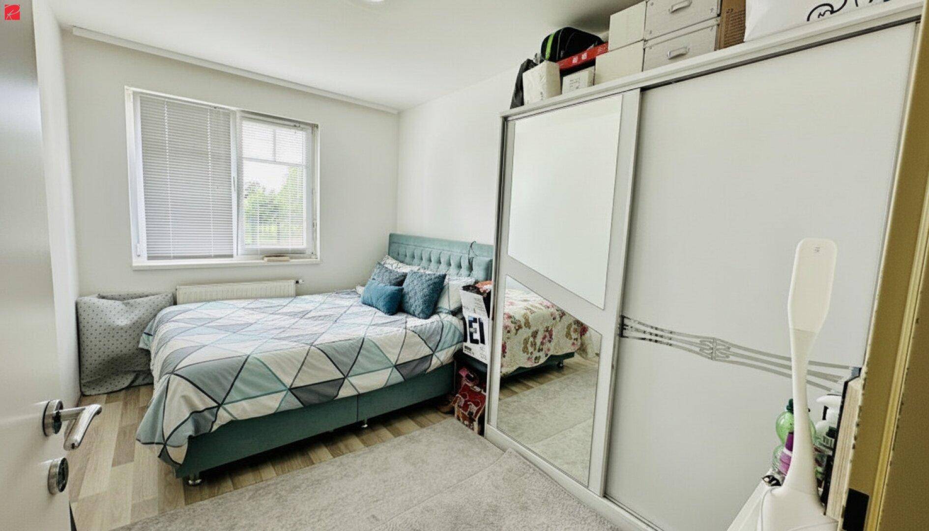 Helles Schlafzimmer mit Doppelbett, Schiebetürenschrank und Fenster mit Jalousien.