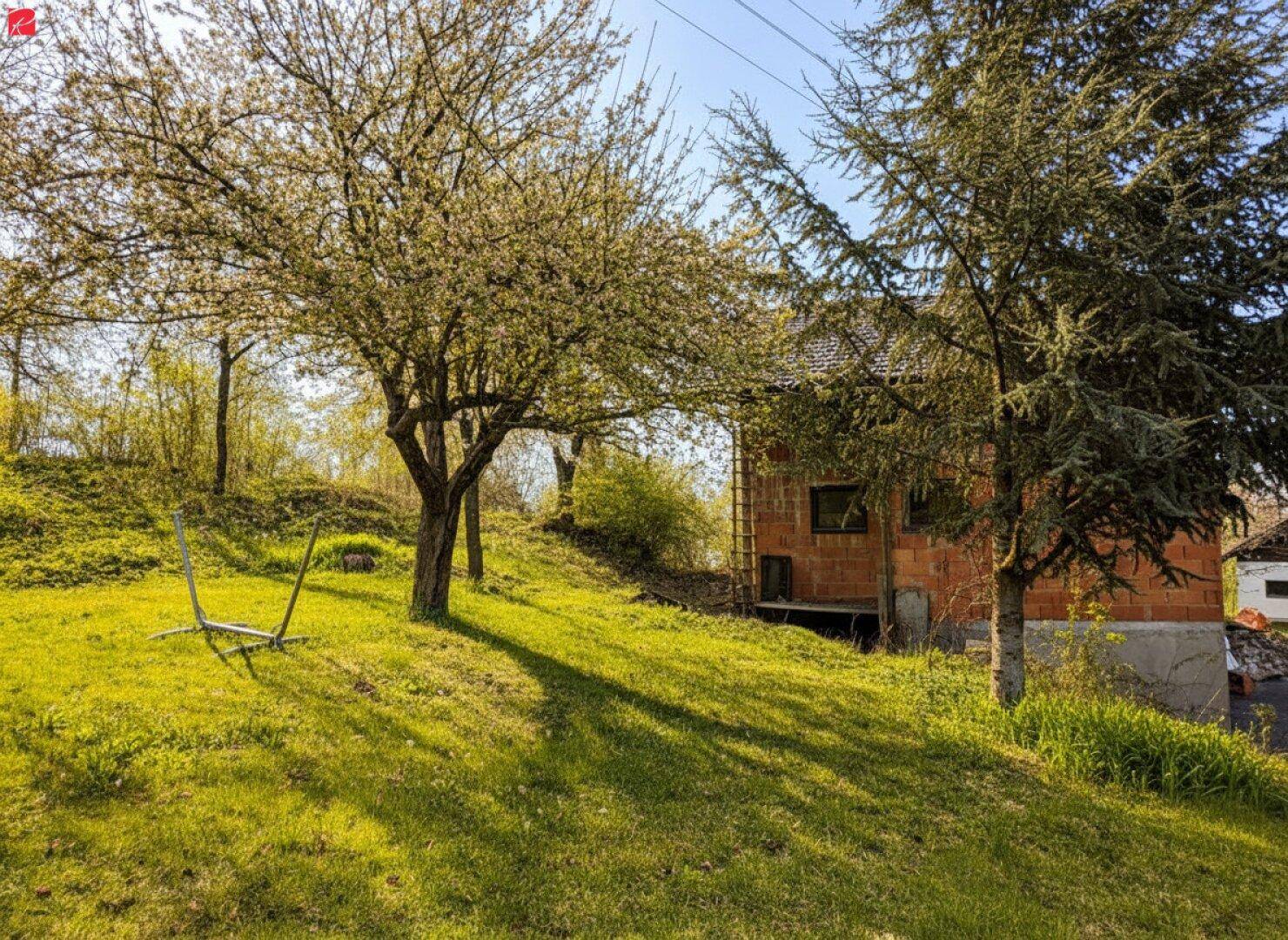 Weitläufiger Garten mit Bäumen und einem weiteren Gebäude im Hintergrund unter blauem Himmel.