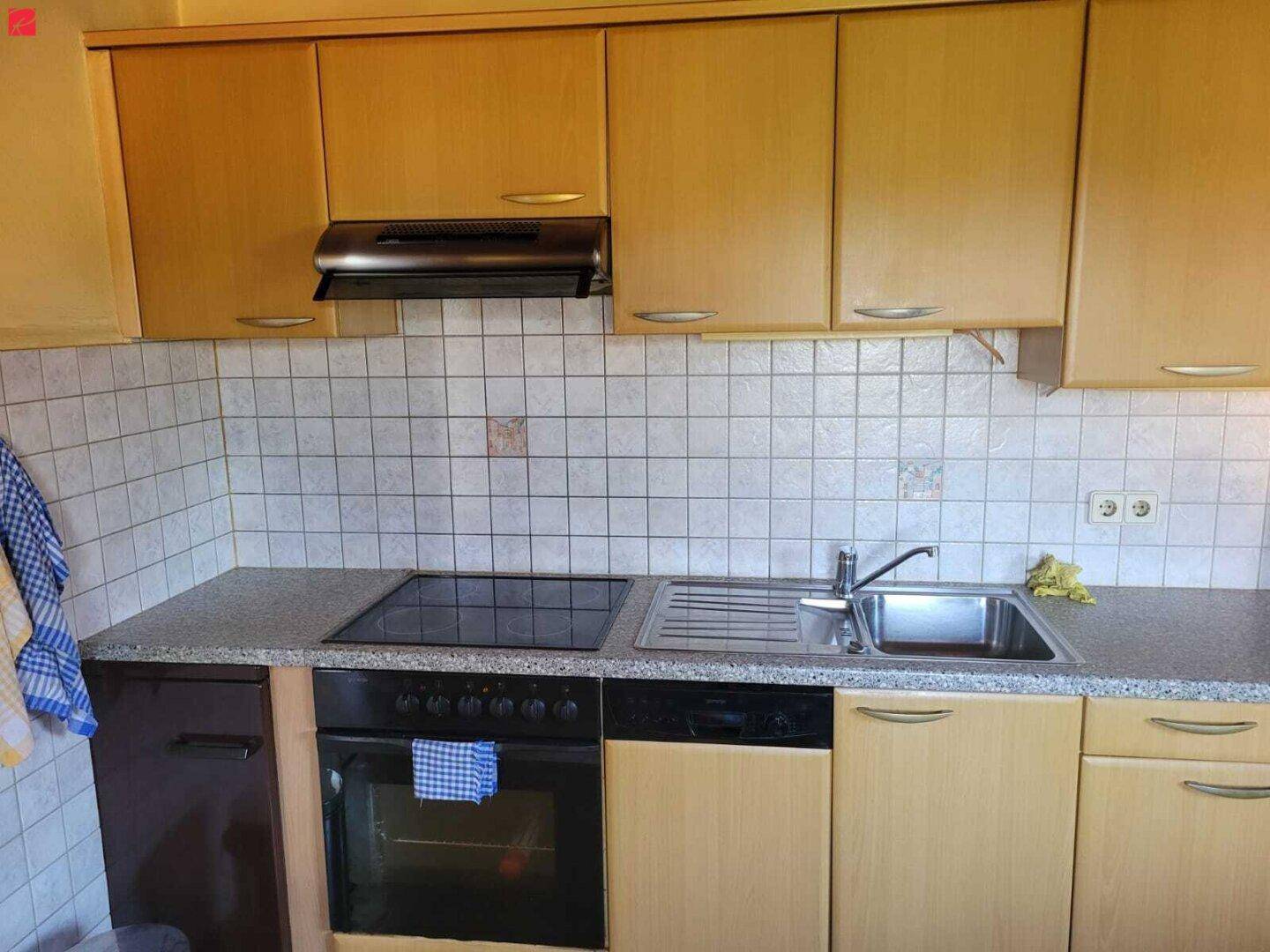 Funktionale Küche mit hellen Holzschränken, Fliesenrückwand und integrierten Geräten.
