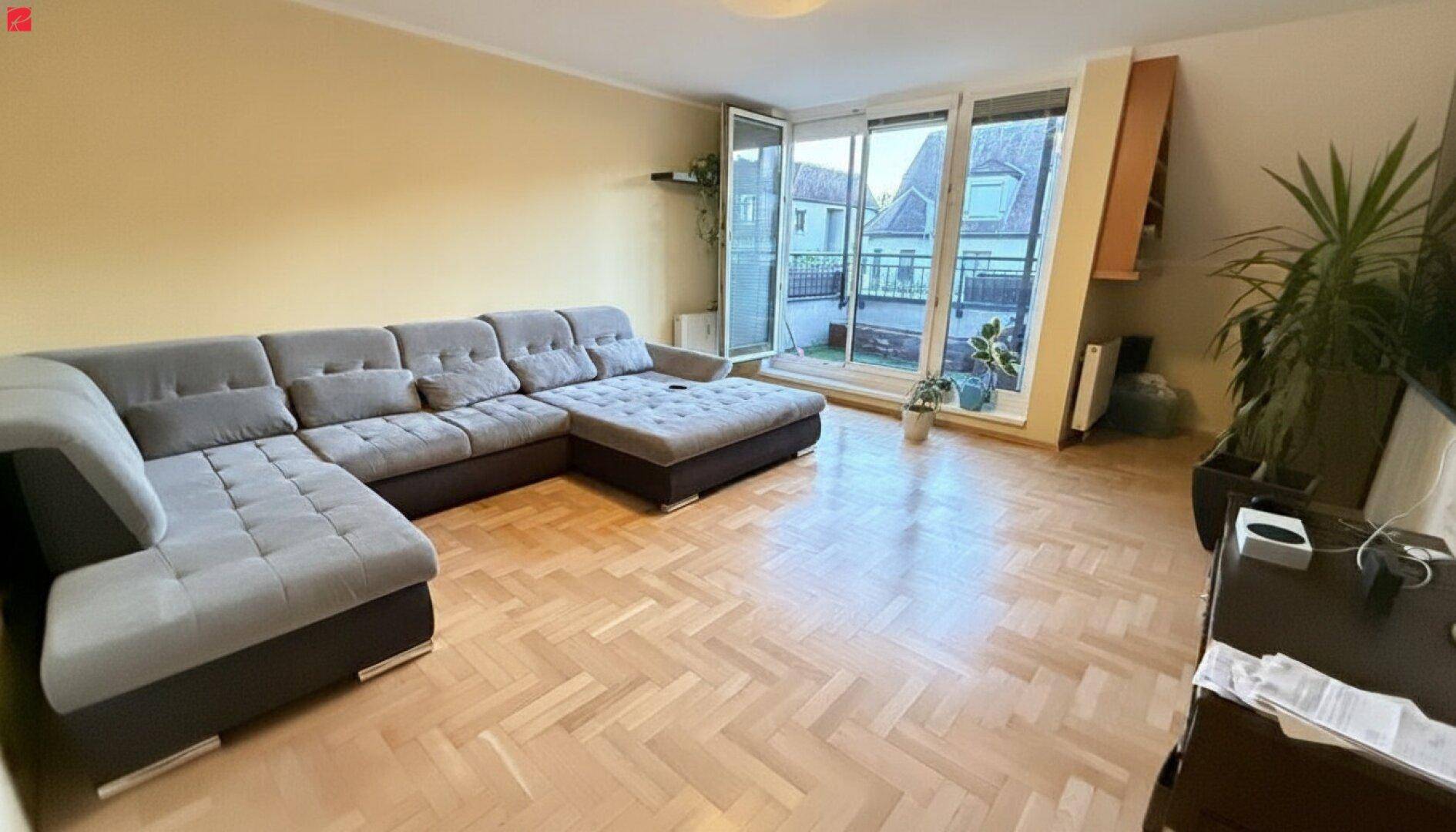 Geräumiges Wohnzimmer mit großem Ecksofa, Parkettboden und Zugang zu einem Außenbereich.