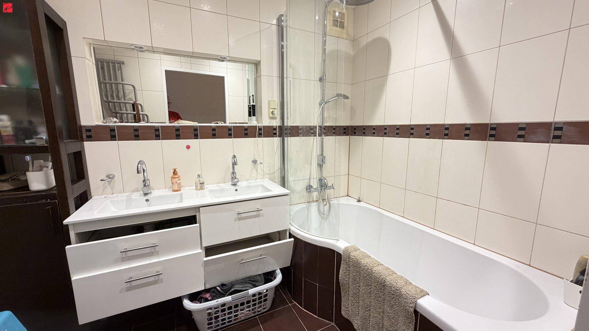 Badezimmer mit Doppelwaschbecken, Badewanne und Duschbereich, gefliest in hellen und dunklen Tönen.