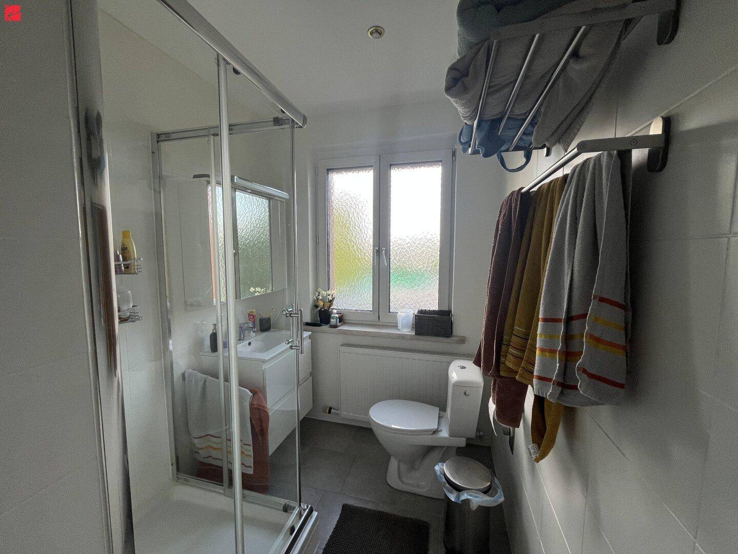 Modernes Badezimmer mit Duschkabine, WC, Waschbecken und Fenster für natürliche Belüftung.