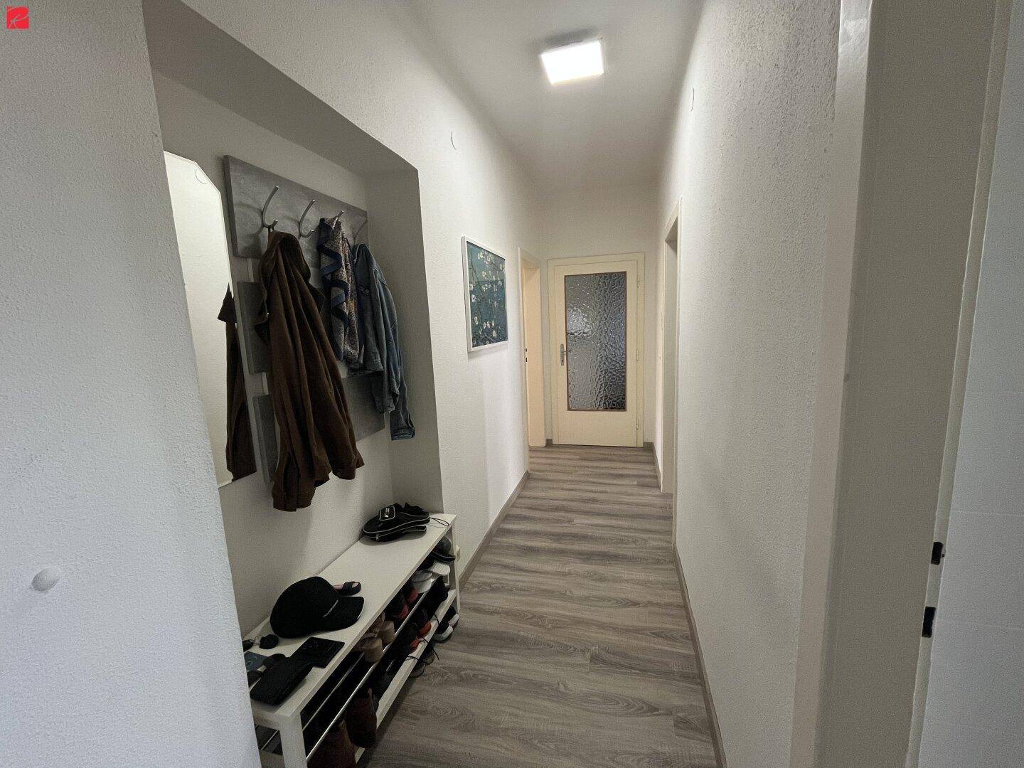 Heller Flur mit Garderobe, Schuhregal und Spiegel, der zu den weiteren Räumen führt.