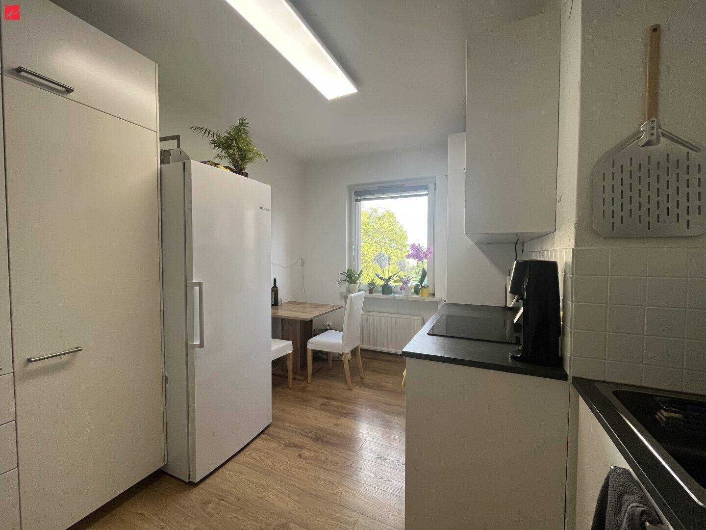 Funktionale Küche mit weißen Schränken, Kühlschrank und kleinem Essbereich am Fenster.