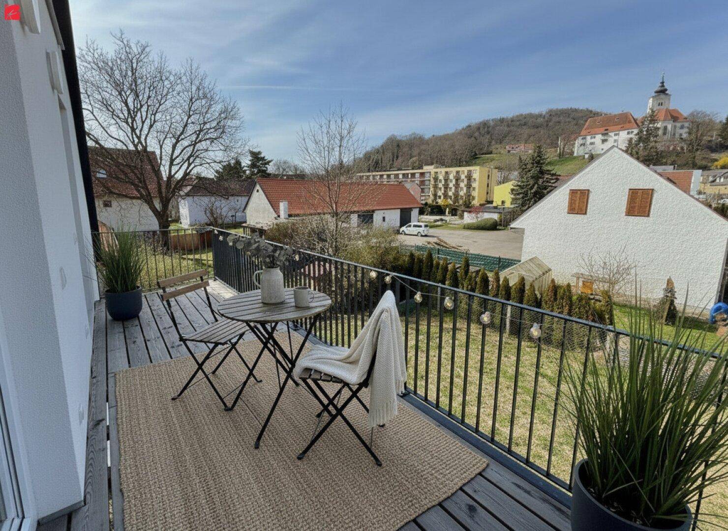 Möblierter Balkon mit Holzboden, Blick auf die Umgebung und eine historische Kirche.