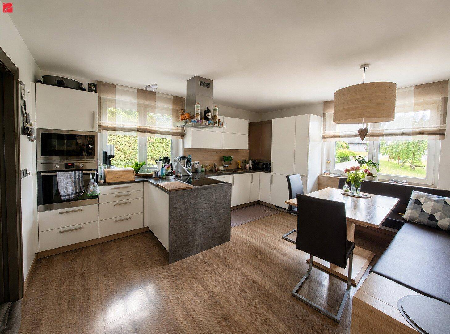 Moderne Wohnküche mit weißen Schränken, Kücheninsel und gemütlichem Essbereich am Fenster.