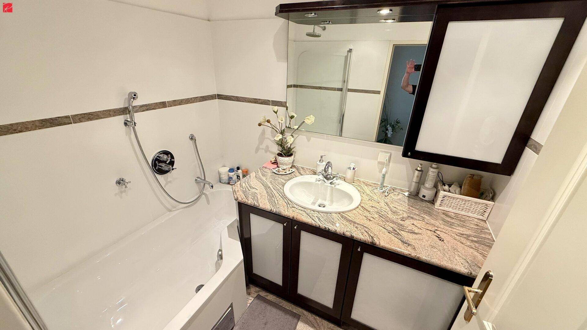 Badezimmer mit Badewanne, Duschfunktion, Einzelwaschbecken und Spiegelschrank.