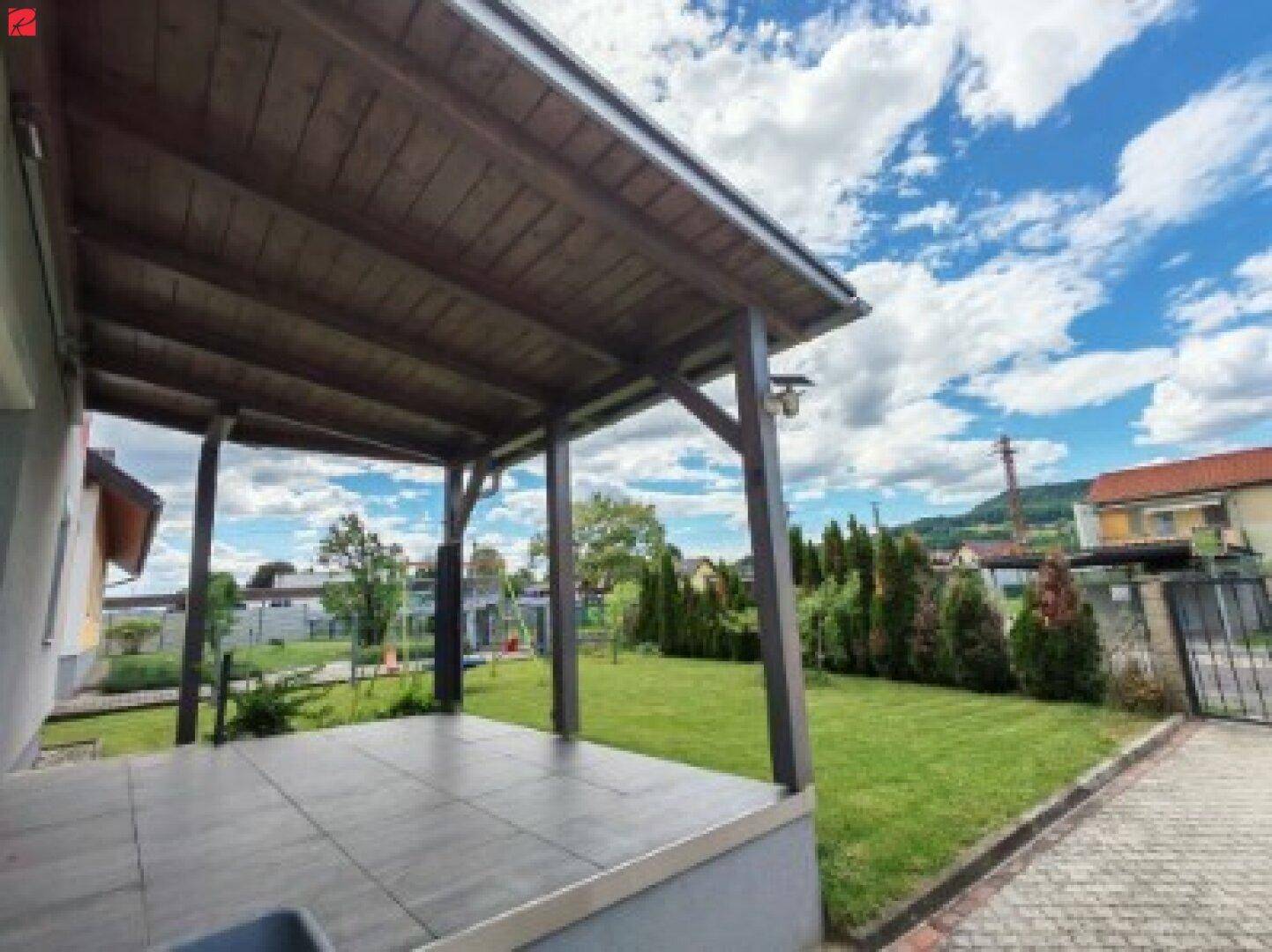 Überdachte Terrasse mit Fliesenboden und Blick auf den Garten mit Spielplatz.