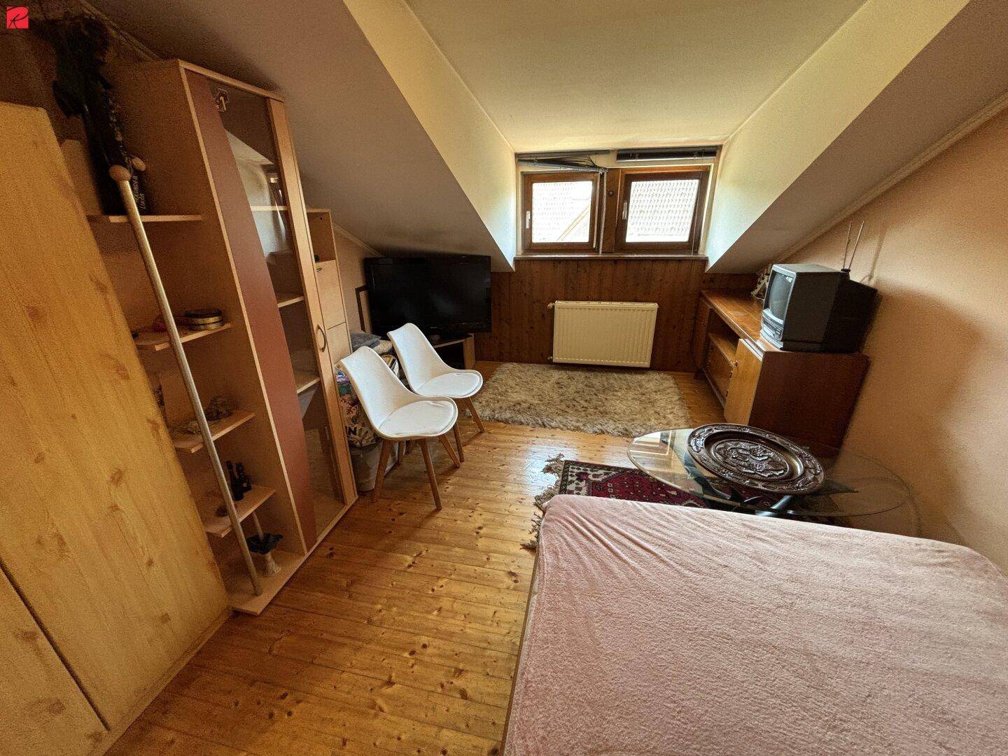 Gemütliches Dachzimmer mit Holzfußboden, Dachschrägen und kleinem Fenster.