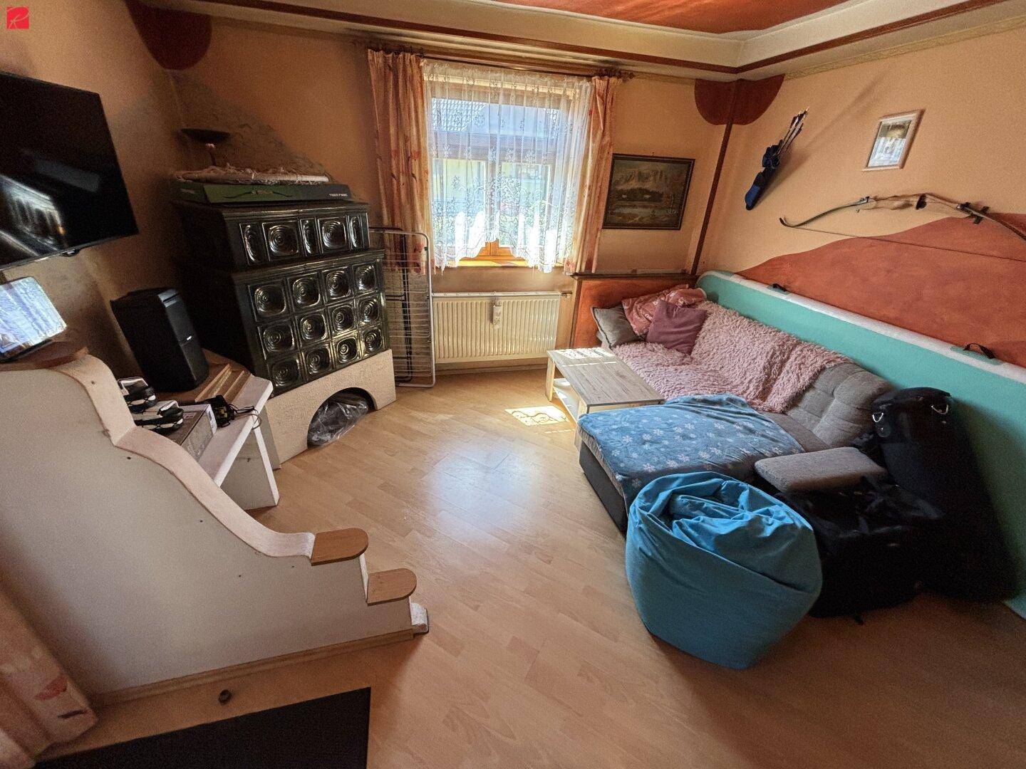 Wohnzimmer mit Kachelofen, Sofa und Holzboden in warmer Farbgebung.