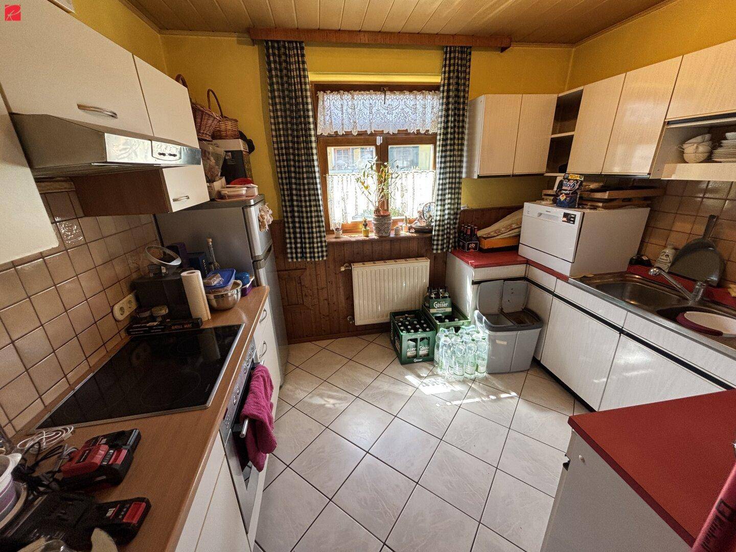 Helle Küche mit weißen Schränken, Fliesenboden und Fenster.