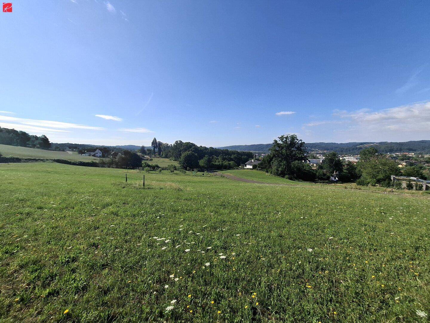 Panoramablick über sanfte Hügel, grüne Wiesen und eine Stadt in der Ferne an einem sonnigen Tag.