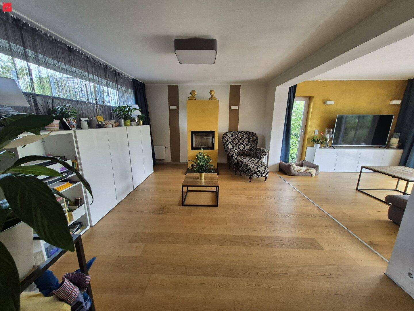 Geräumiges Wohnzimmer mit Holzboden, modernem Kamin und farbenfrohen Akzenten, hell und einladend.