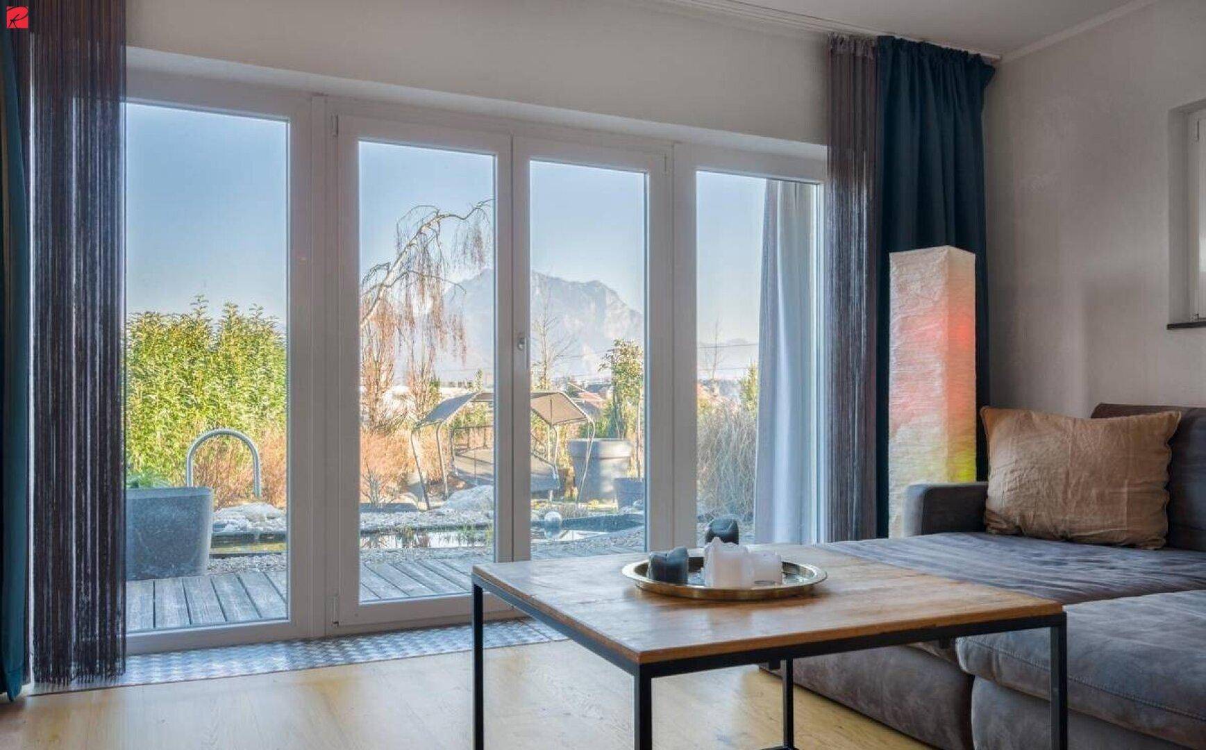 Helles Wohnzimmer mit großen Fenstern, die einen Blick auf die Terrasse und die Berge bieten.