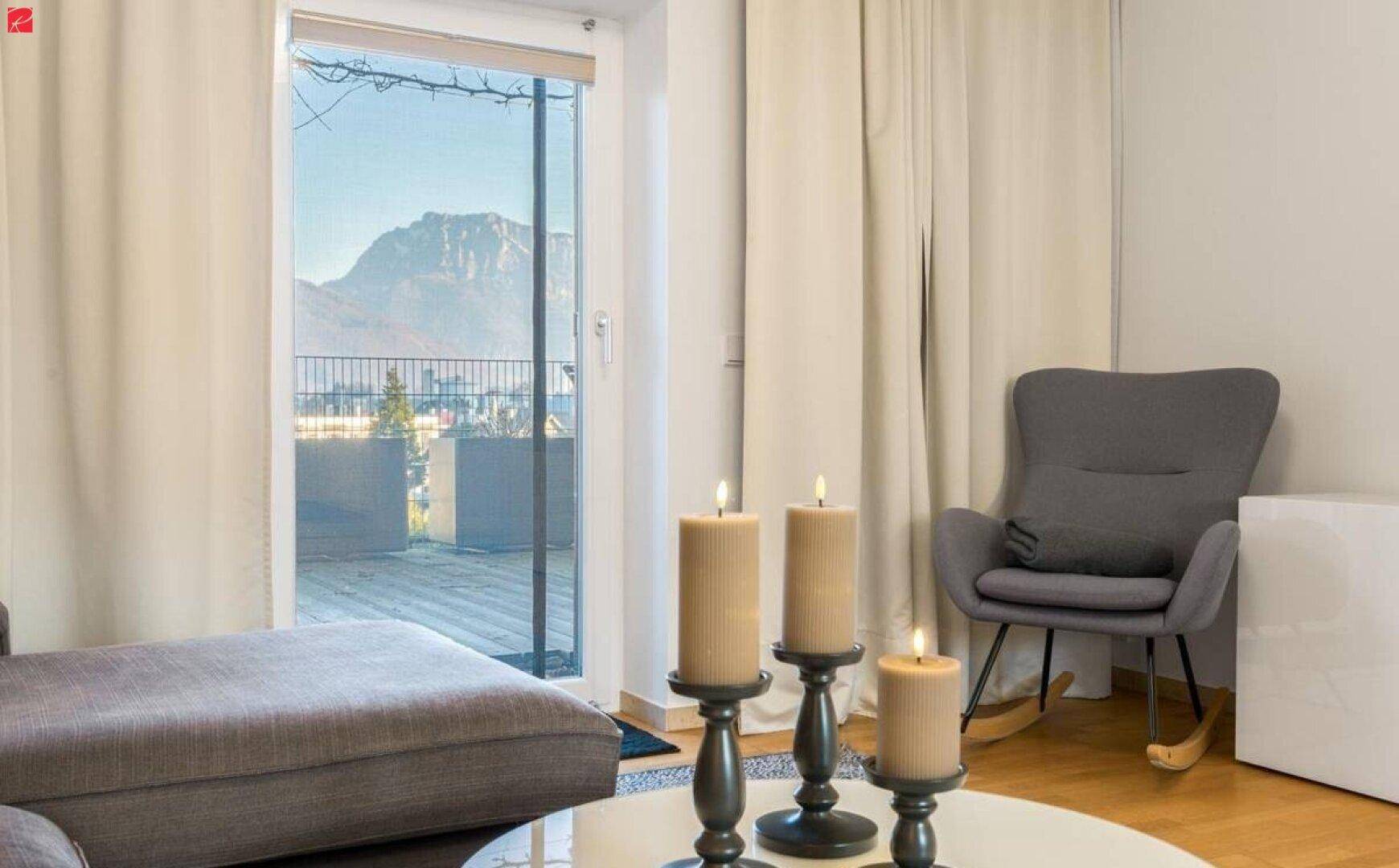 Gemütlicher Wohnbereich mit Sofa, Schaukelstuhl und Zugang zu einem Balkon mit Bergblick.