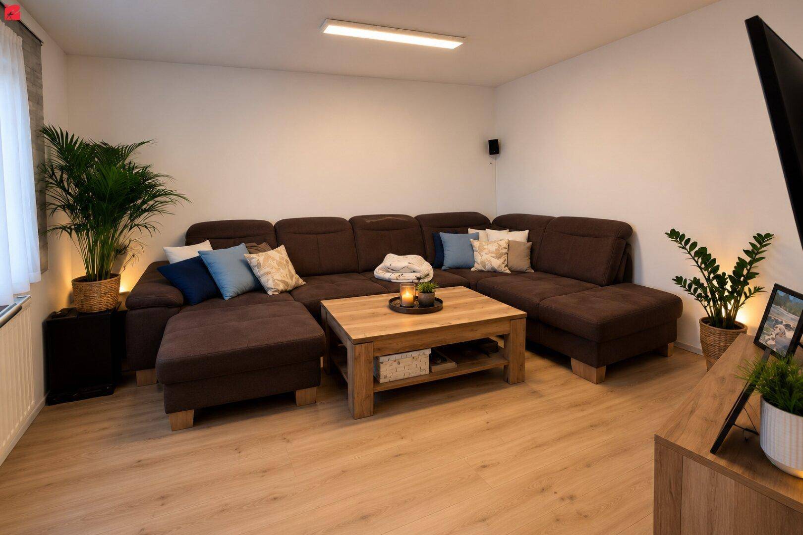 Gemütliches Wohnzimmer mit großem Ecksofa, Holztisch und Laminatboden, dekoriert mit Pflanzen.