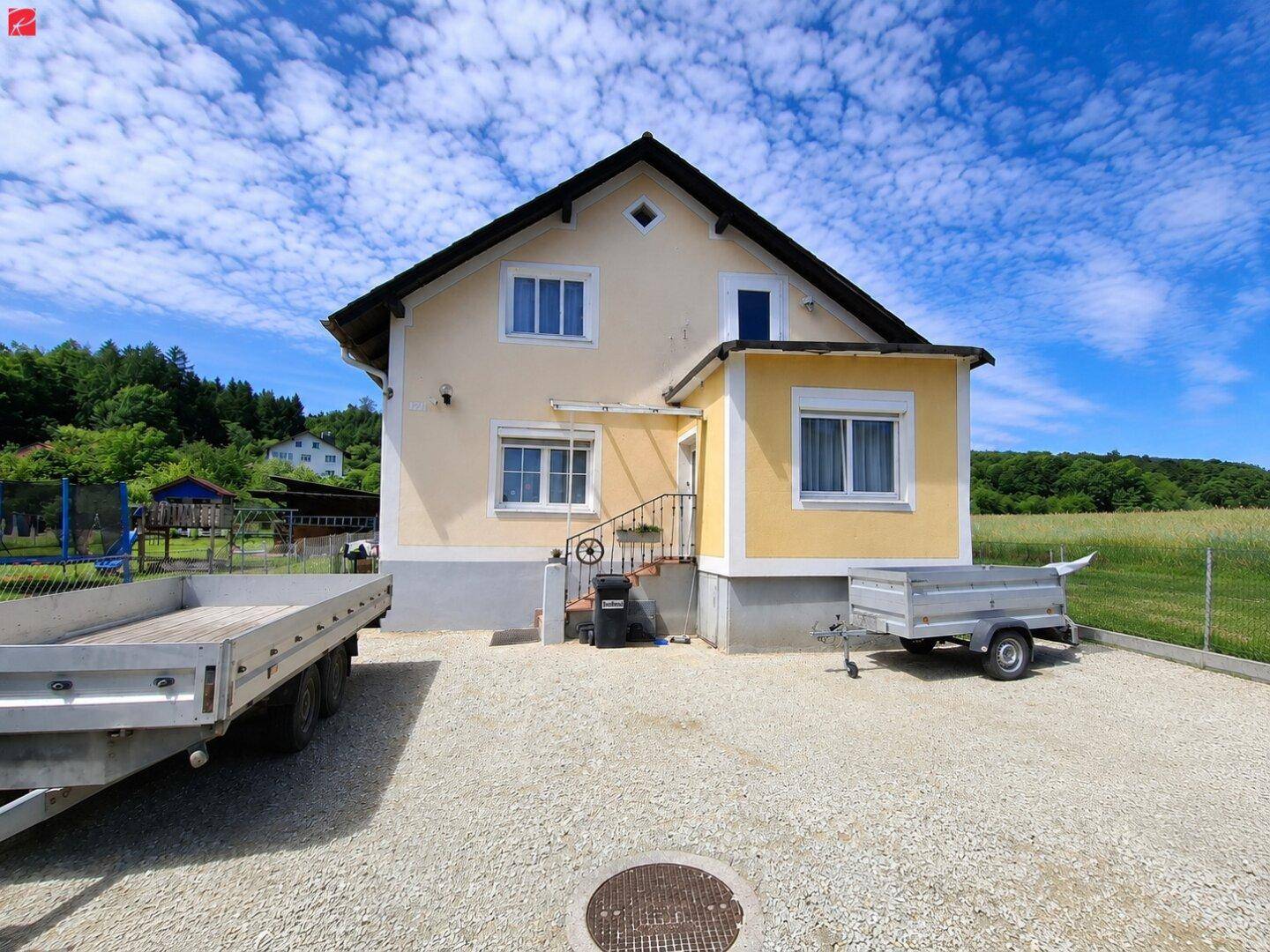 Rückansicht eines Einfamilienhauses mit Kiesauffahrt und einem Anhänger unter blauem Himmel.