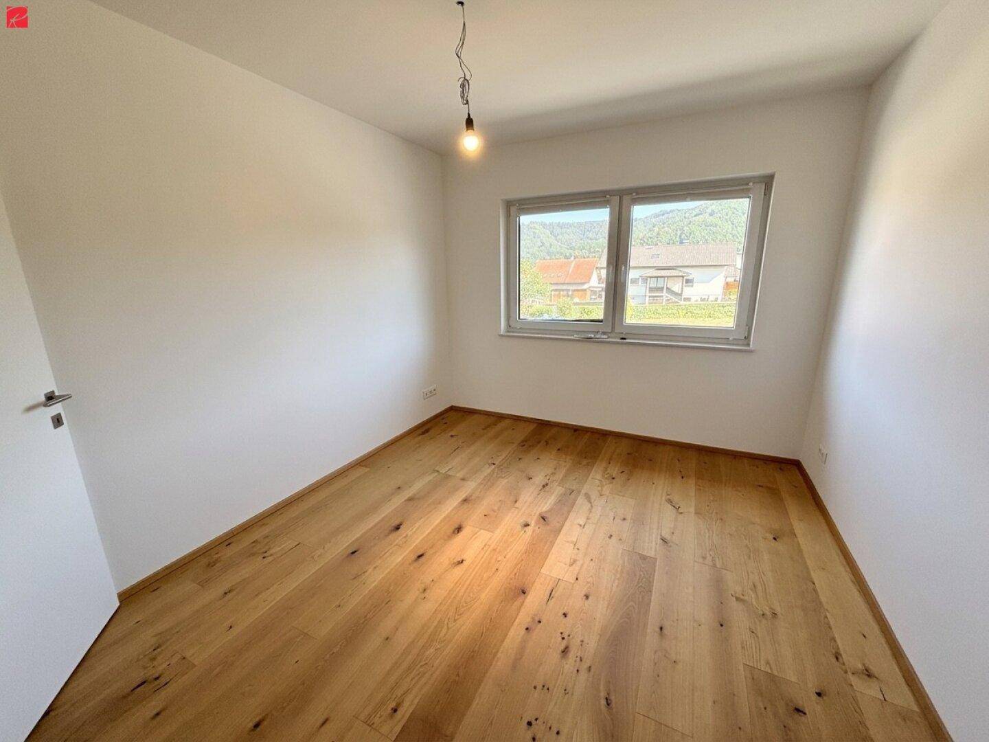 Helles Zimmer mit Holzdielenboden und Fenster, das einen Ausblick auf die umliegende Wohngegend bietet.