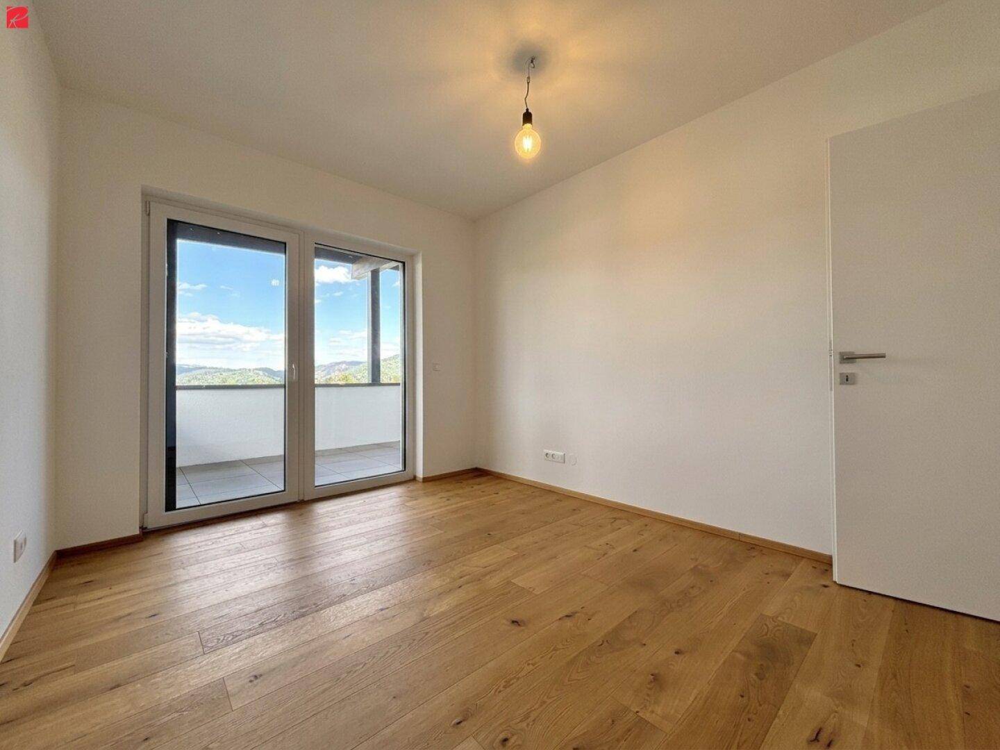 Geräumiges Schlafzimmer mit hellem Holzboden und großer Balkontür, die viel Tageslicht hereinlässt.
