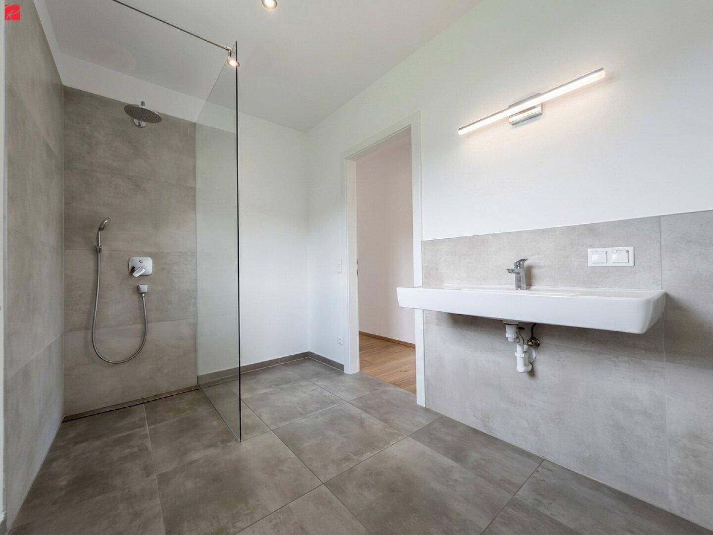 Modernes Badezimmer mit grauen Fliesen, einer begehbaren Dusche und einem stilvollen Waschtisch.