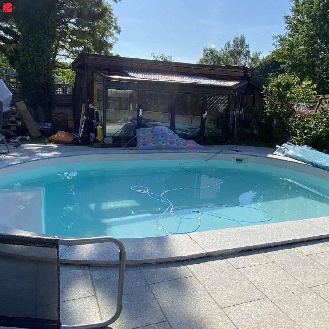 Außenbereich mit ovalem Pool, gepflasterter Terrasse und einem Gartenhaus im Hintergrund.