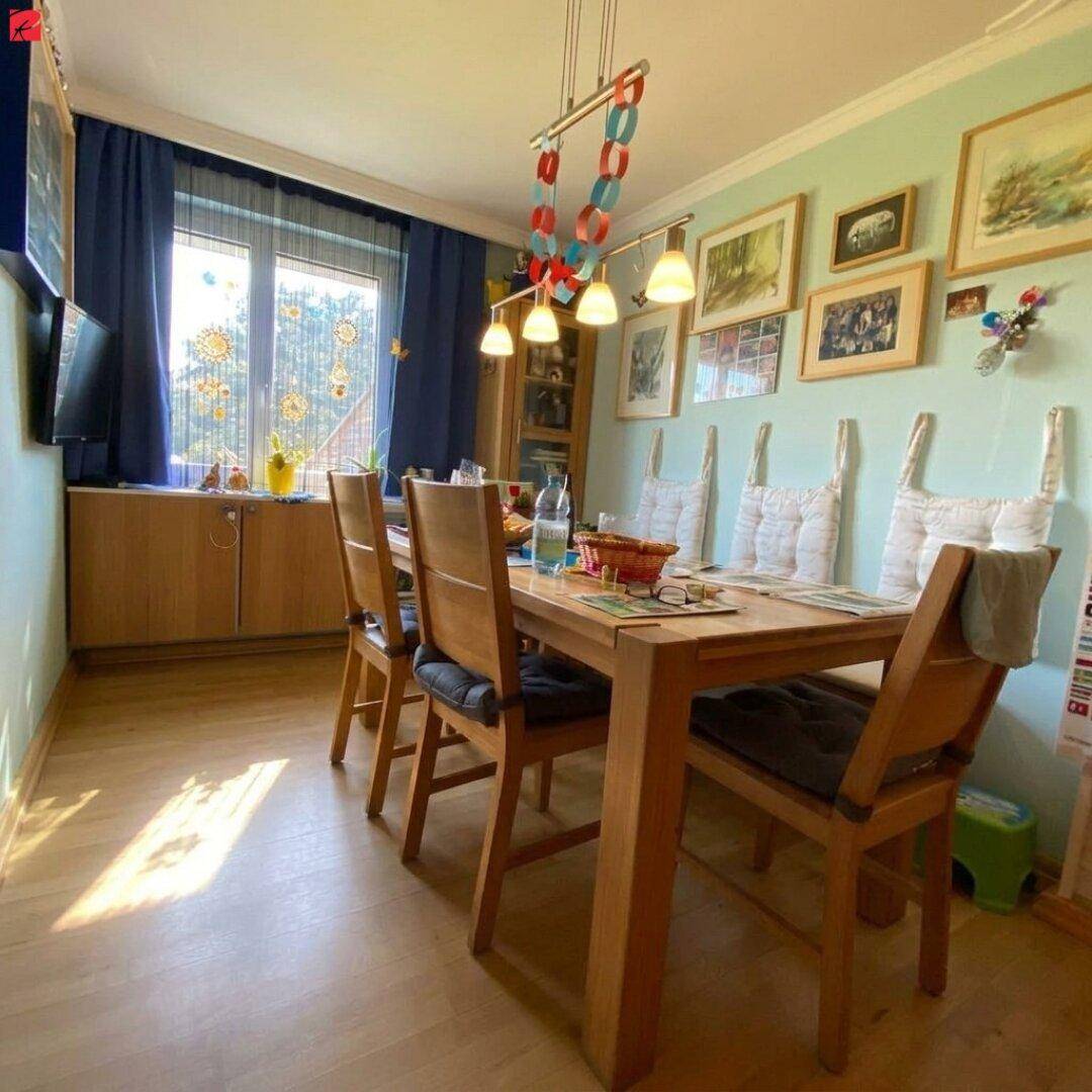 Gemütliches Esszimmer mit Holztisch, Stühlen und Bildern an der hellgrünen Wand.
