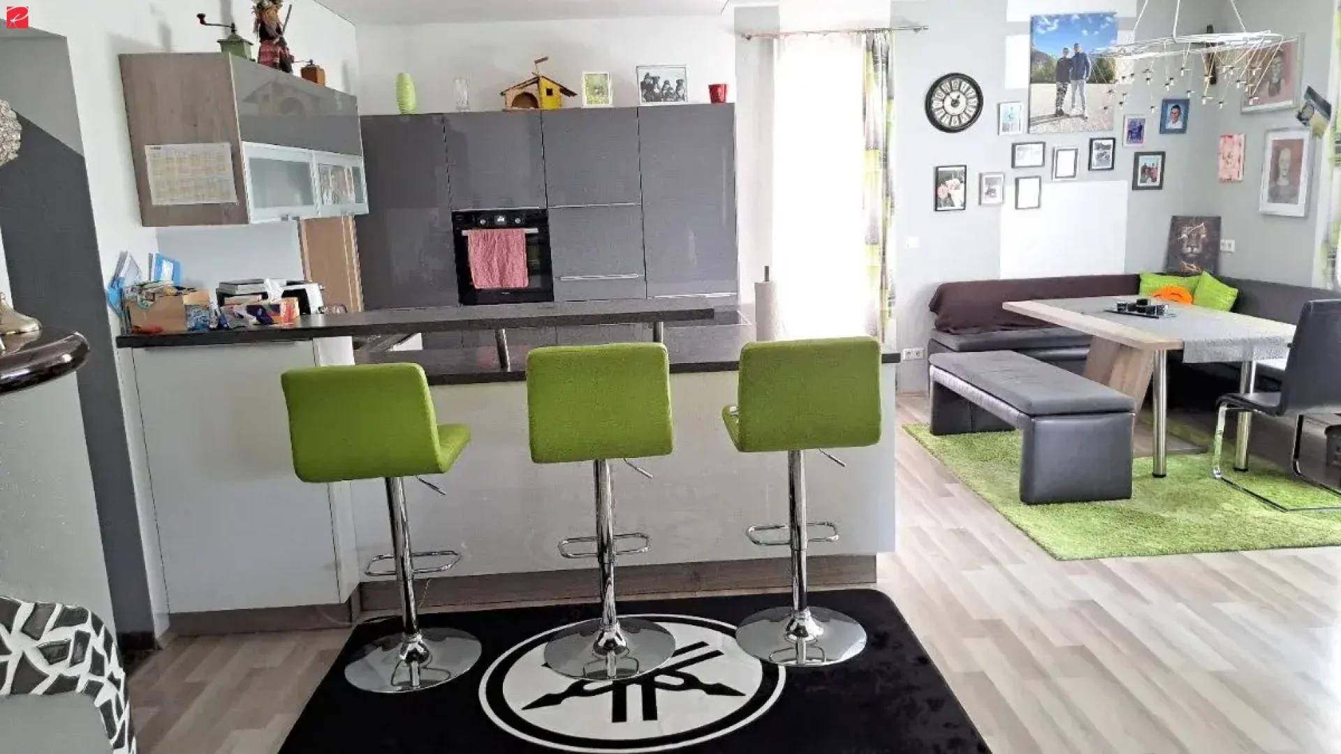 Moderne Küche mit Frühstücksbar und offenem Übergang zum Essbereich, ausgestattet mit grünen Barhockern.