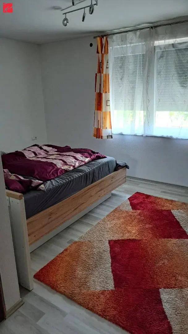 Schlafzimmer mit einem Holzbett, einem farbenfrohen Teppich und einem Fenster mit Rollläden für Privatsphäre.