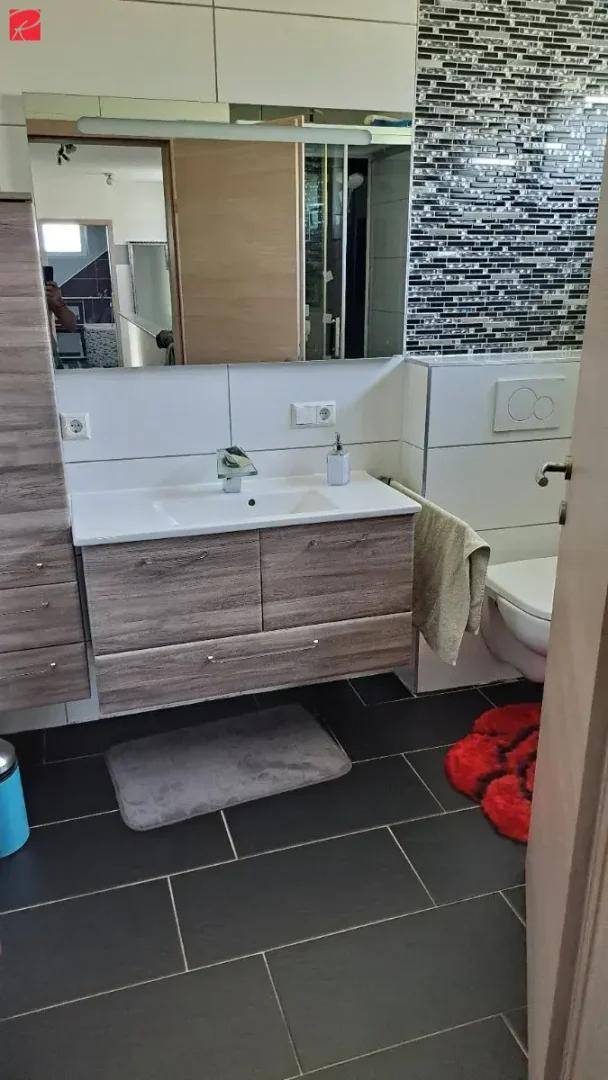 Modernes Badezimmer mit Einzelwaschbecken, Spiegelschrank und Toilette, ausgestattet mit dunklen Bodenfliesen.