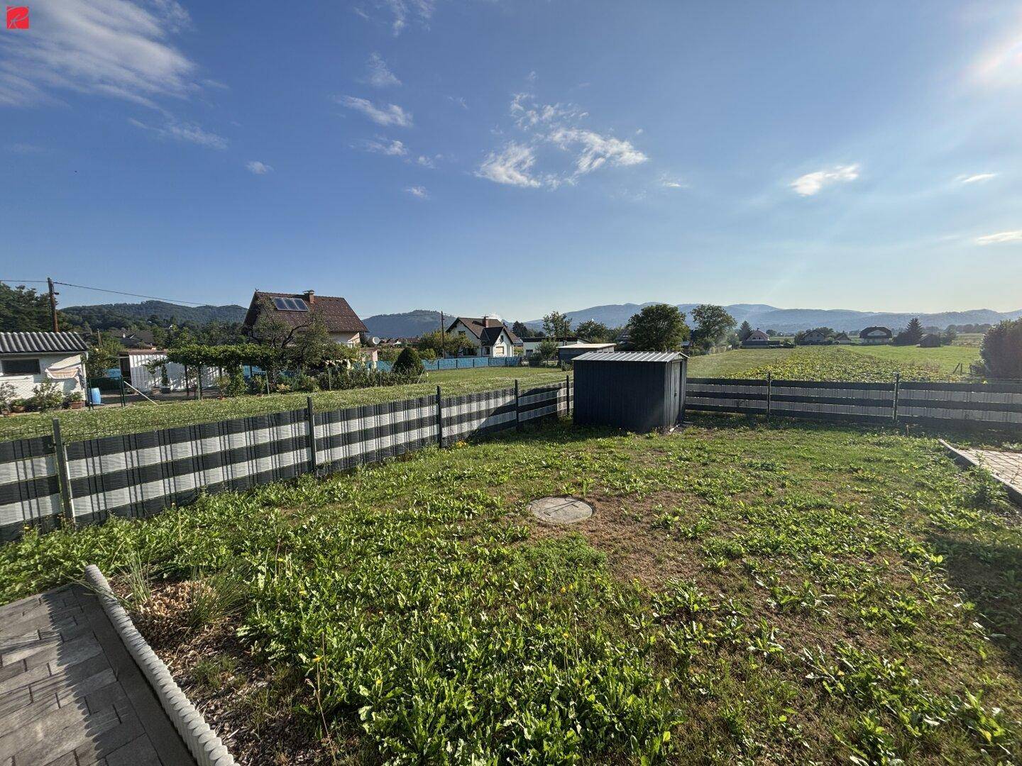 Gepflegter Gartenbereich mit Rasenfläche, kleinem Geräteschuppen und Blick auf die Landschaft.
