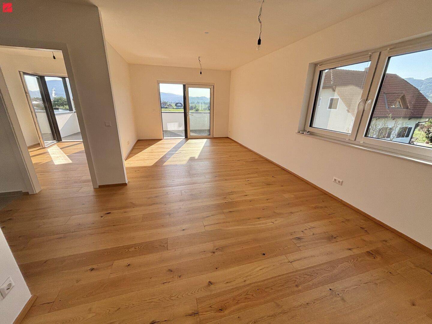 Heller, leerer Wohnraum mit neuem Holzboden und Zugang zu einem Balkon mit Bergblick.