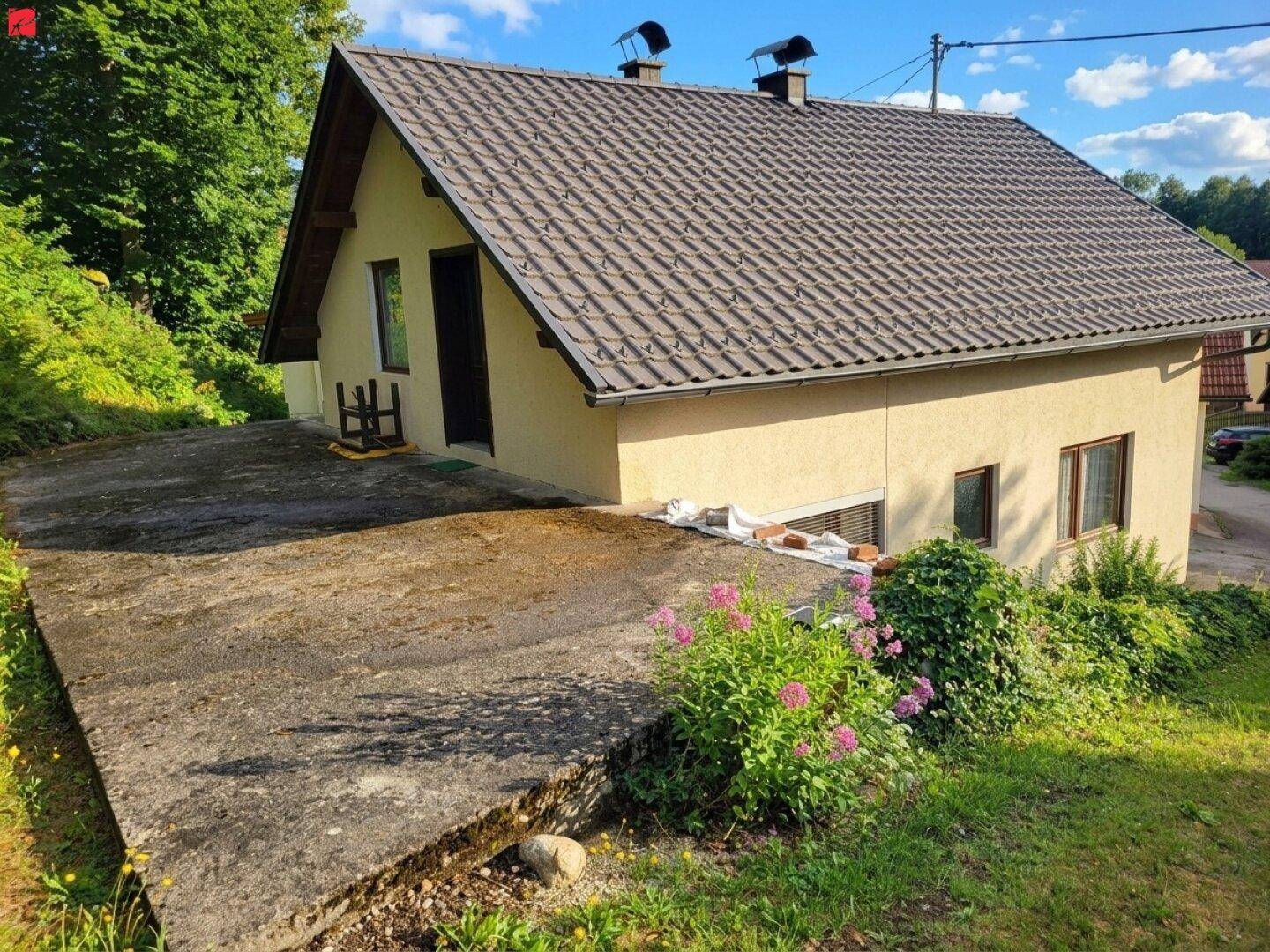 Seitenansicht des Hauses mit Satteldach und großer Betonfläche im Vordergrund.