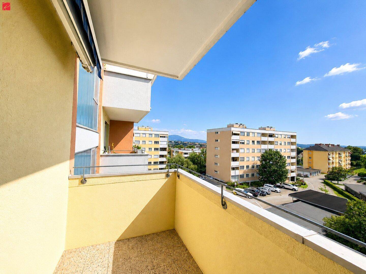 Sonniger Balkon mit Markise und einem weiten Blick über die Stadt und die umliegende Berglandschaft.