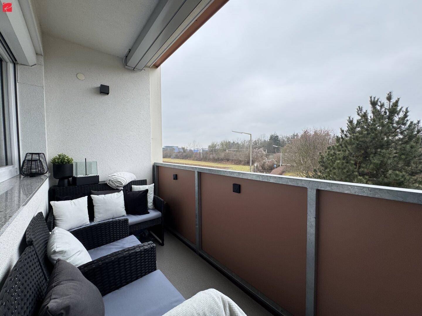 Gemütlicher Balkon mit Rattanmöbeln, Markise und Blick ins Grüne.