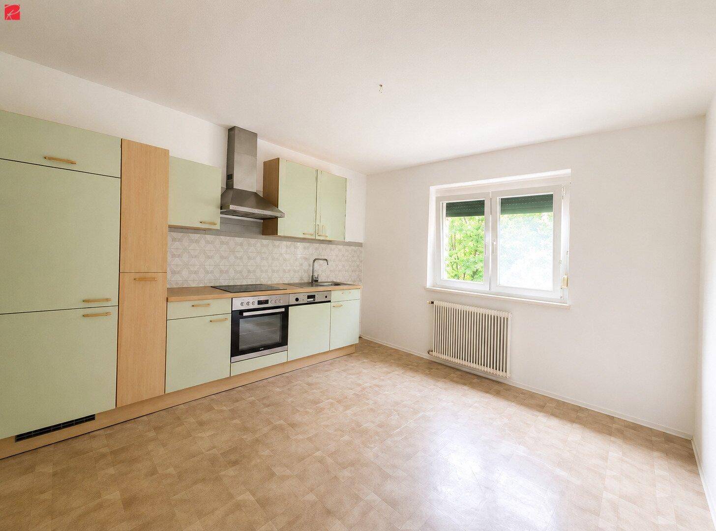 Funktionale Küche mit hellgrünen und holzfarbenen Schränken sowie einem Fenster mit Blick ins Grüne.